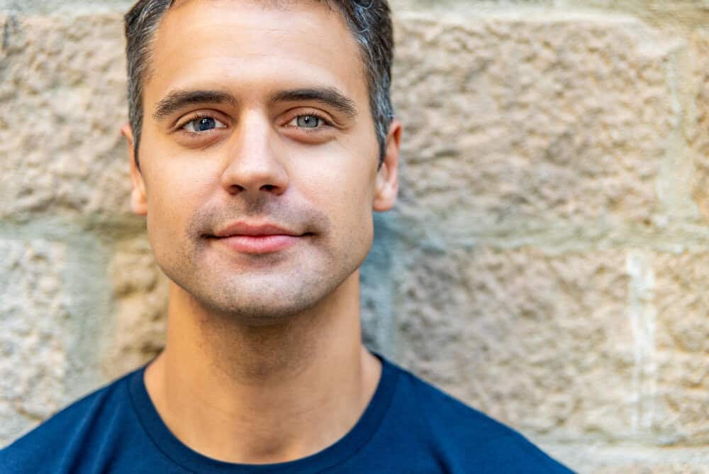 Low angle photo of confident man with blue eyes and short hair in front of brick wall, promoting merchant services solutions.