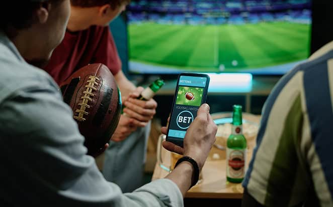 Betting app with sports betting on a mobile device in a sports bar setting, featuring drinks and a TV screen in the background.