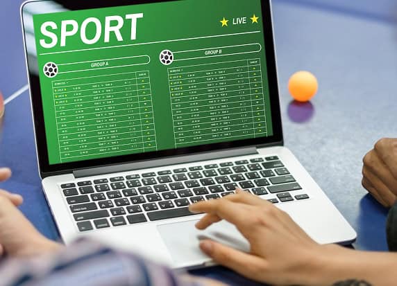 Laptop displaying live sports scores and betting odds, with focus on online sports betting and merchant services.