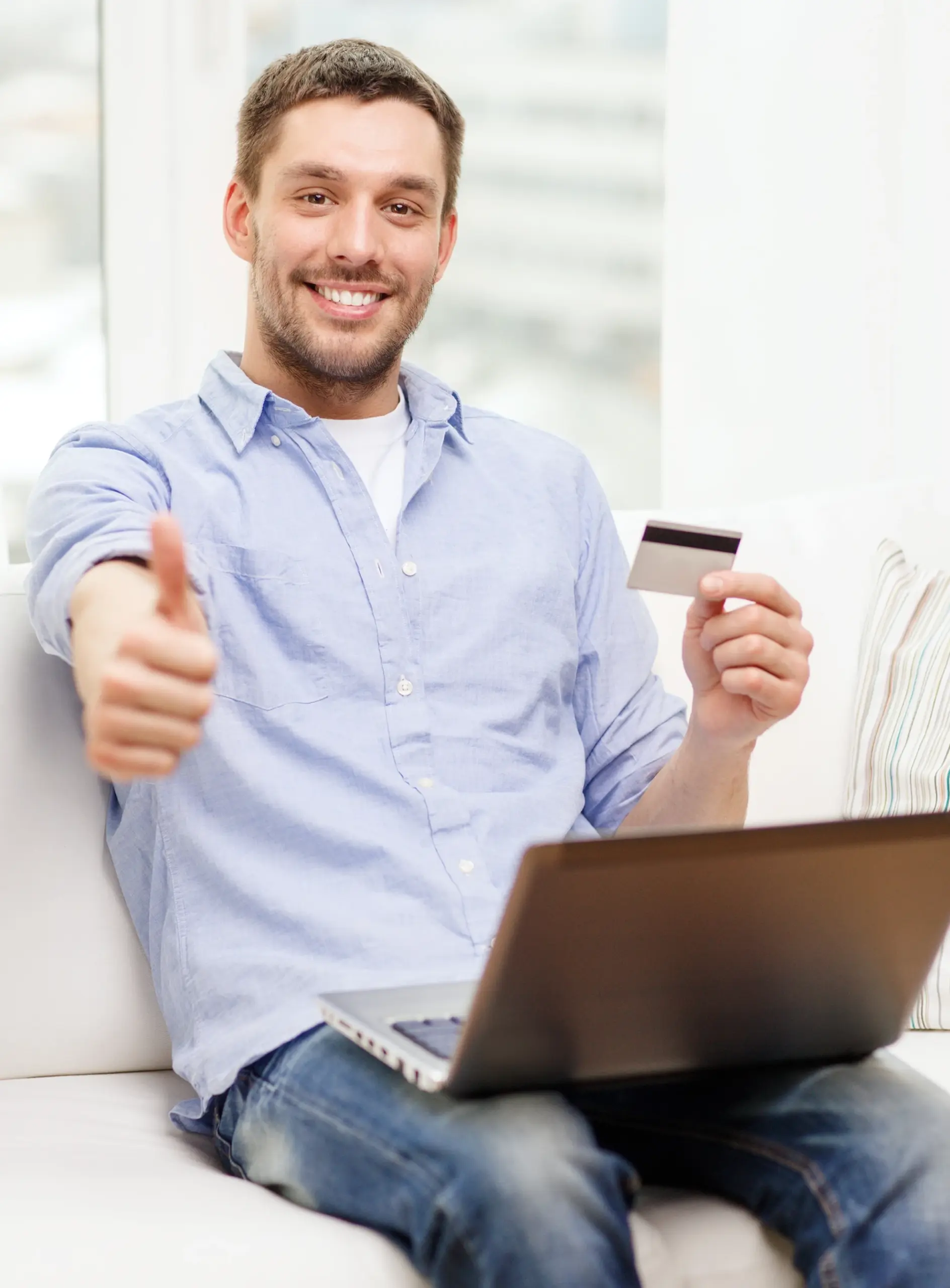 Smiling business owner holding a payment card beside a laptop while giving a thumbs-up