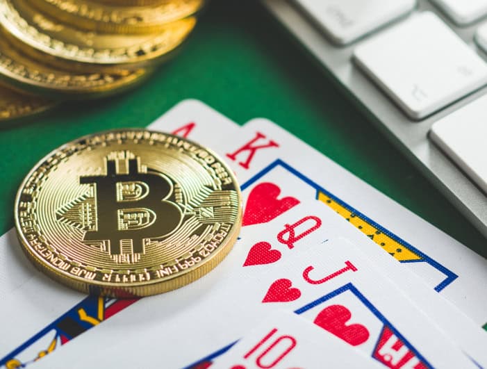 Bitcoin cryptocurrency coins and playing cards on a green surface with a keyboard in the background.