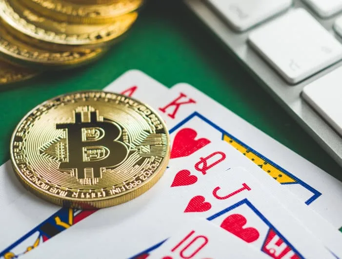 Bitcoin cryptocurrency coins and playing cards on a green surface with a keyboard in the background.