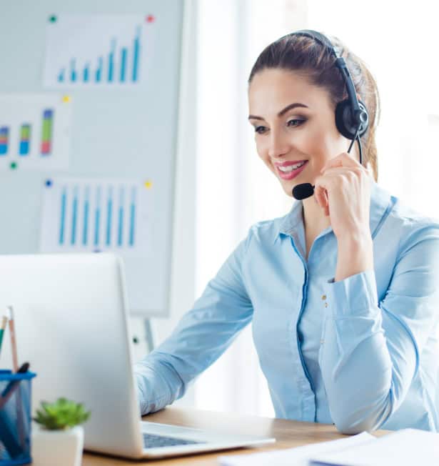Professional customer support representative with headset working at laptop in office environment.