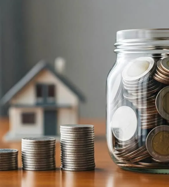 Stacks of coins and a glass jar for savings with a house model in the background, emphasizing financial growth with Host Merchant Services.