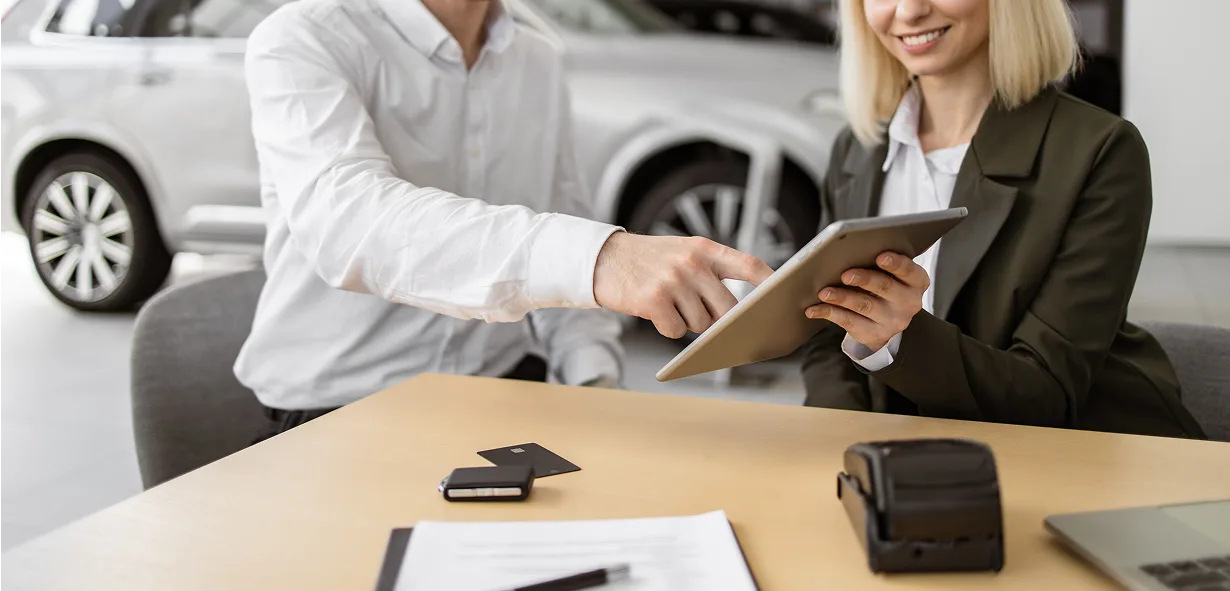 Mobile payment transaction at car dealership with friendly staff.