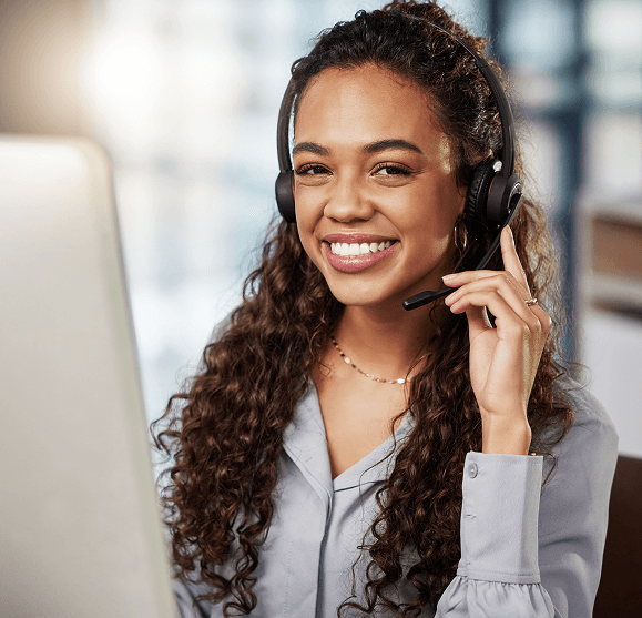 Customer service representative wearing headset, working on laptop at call center or support desk.
