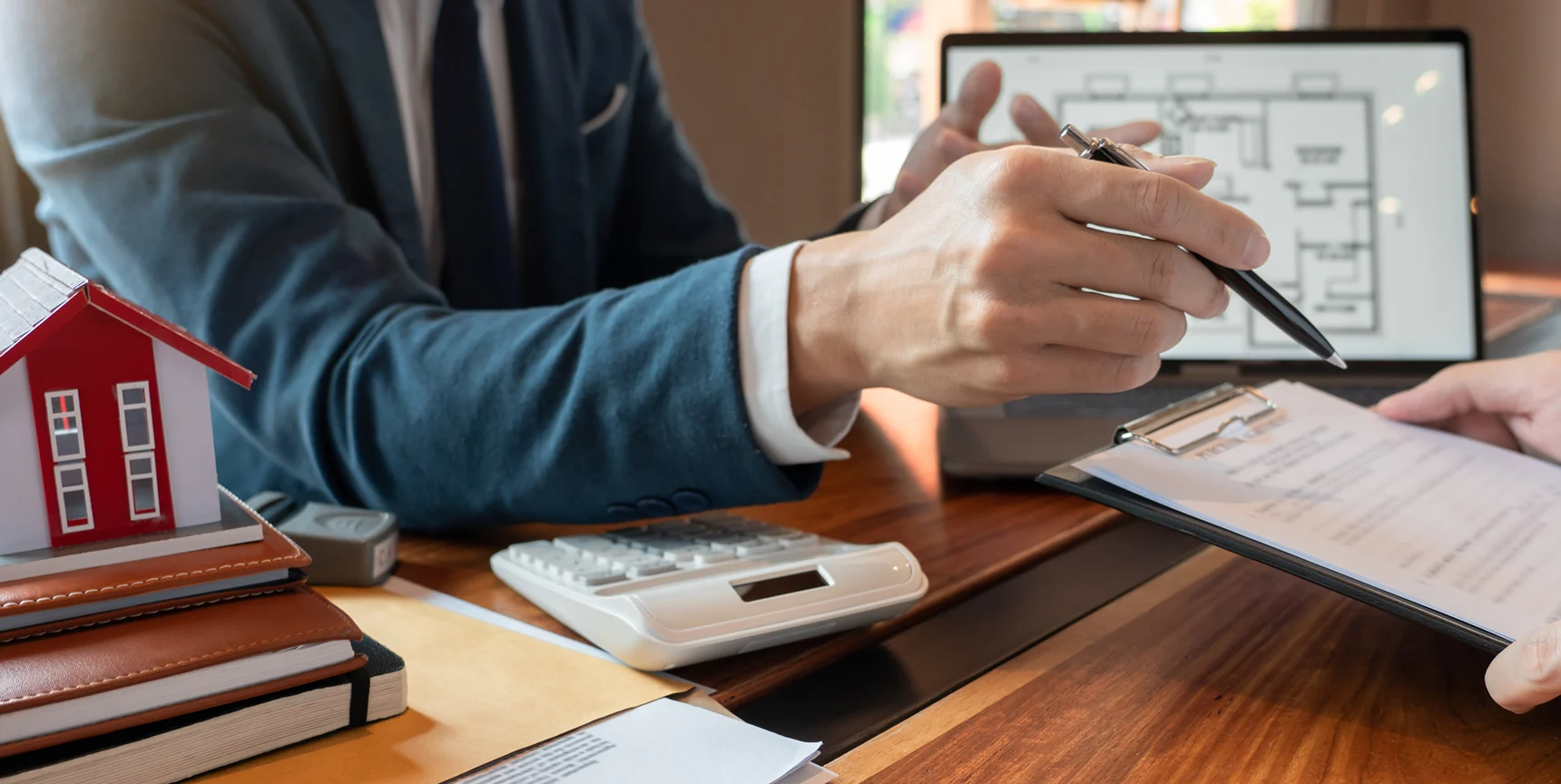 Real estate professional reviewing property documents with a model home, calculator, and digital property plans