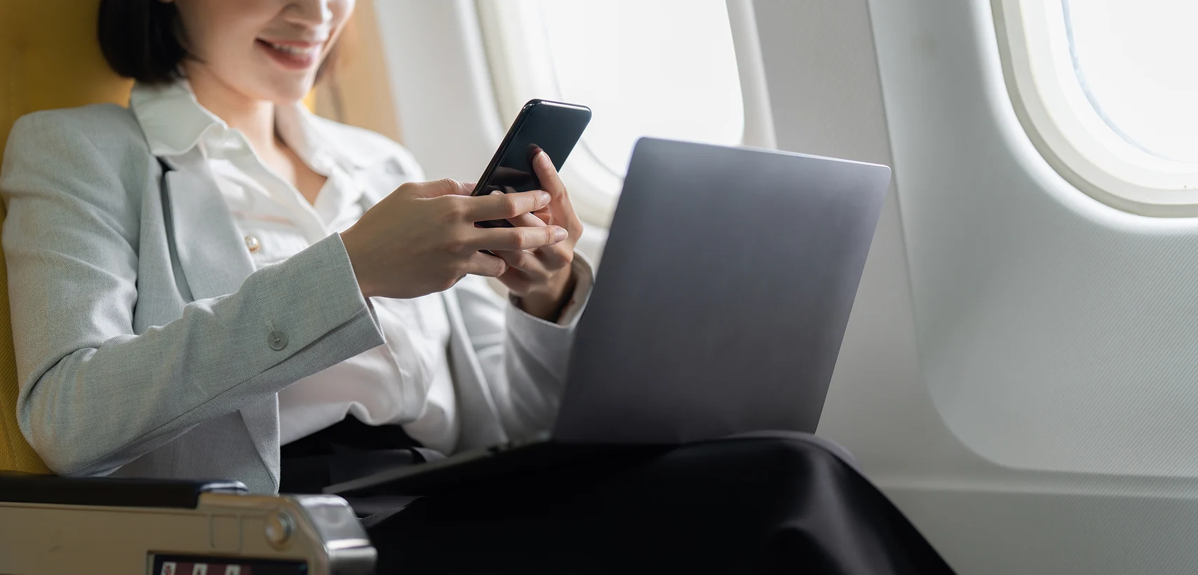 Businesswoman using a laptop on private jet for payment processing and merchant services.