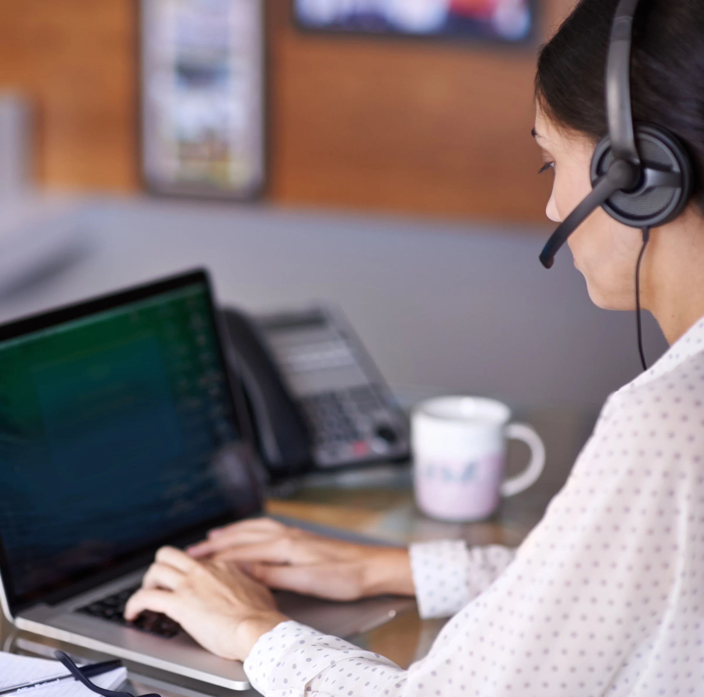 Customer support representative wearing a headset and using a laptop to assist businesses with KORONA POS systems and payment processing