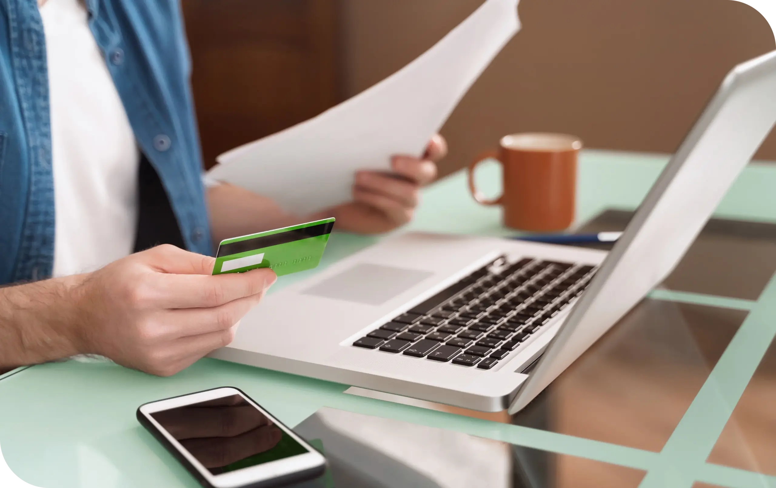 Business owner holding a credit card and reviewing documents beside a laptop while applying for a credit repair merchant account