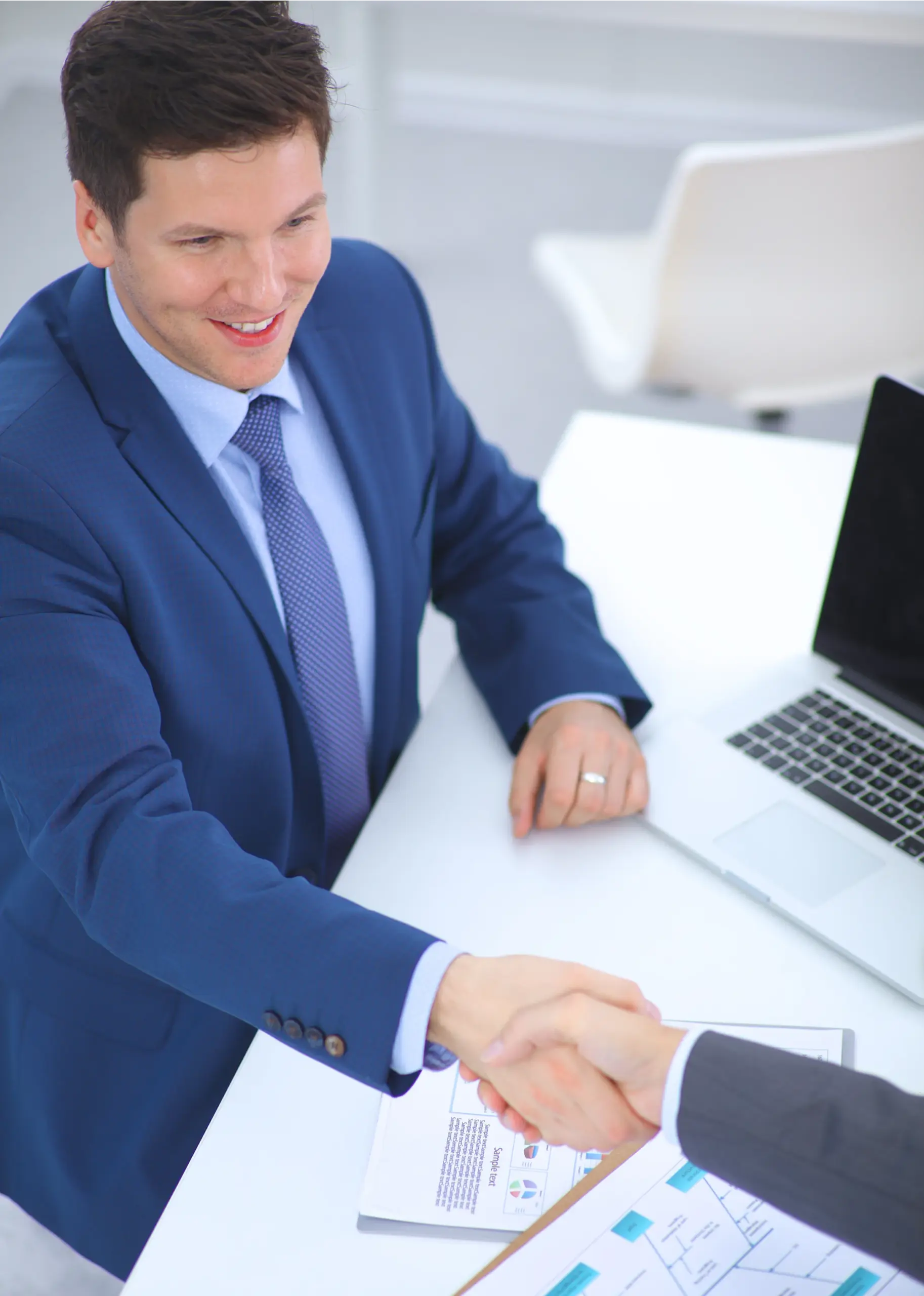 Business professional shaking hands with a client beside a laptop and financial documents, representing a business funding agreement