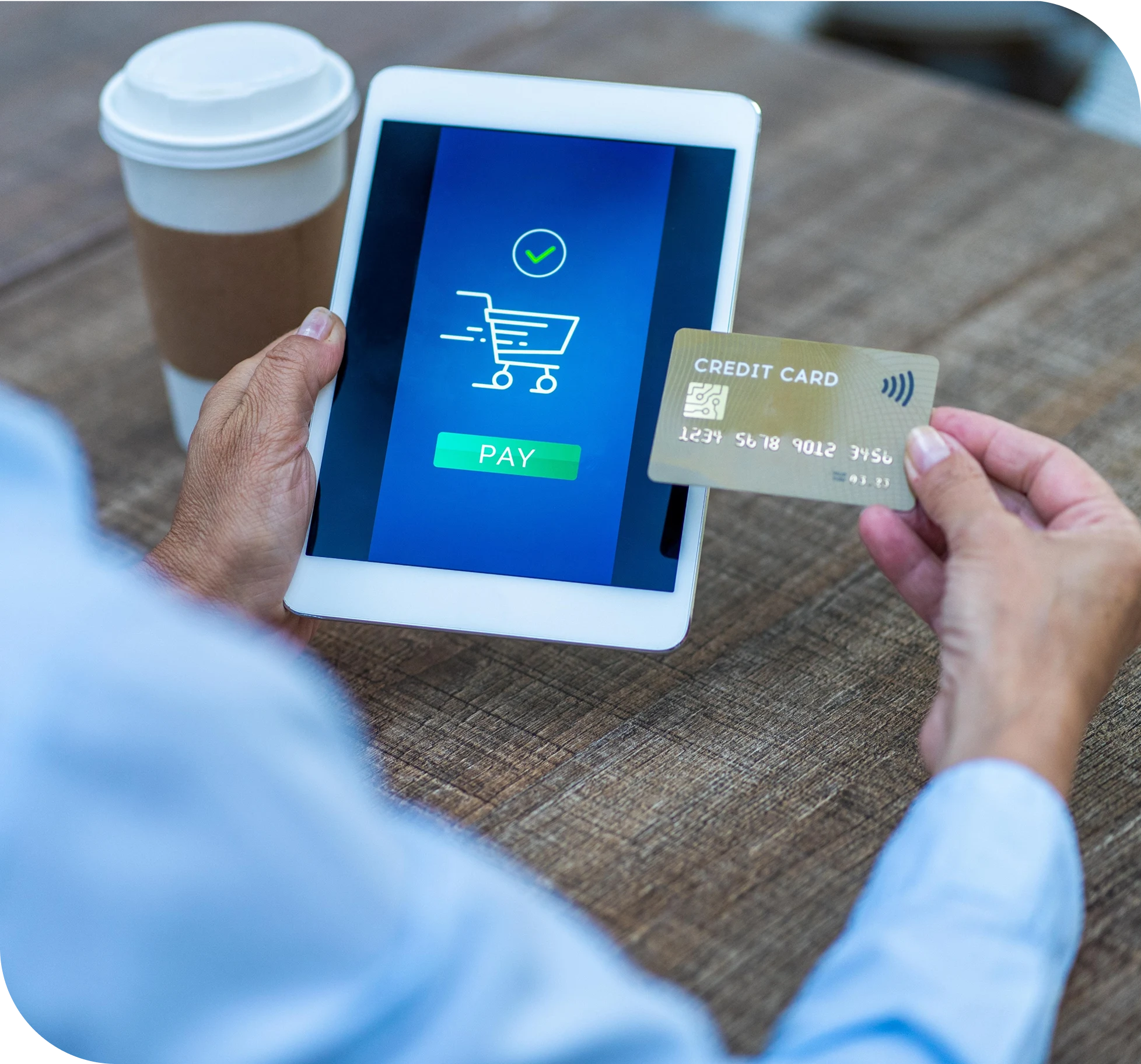 Customer holding a credit card beside a tablet displaying a secure online payment screen with a shopping cart and verification checkmark
